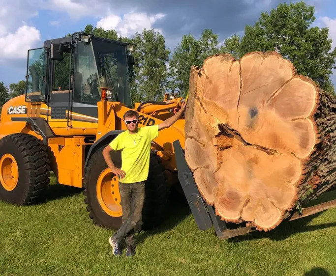 Tip Top Timber Co. crew member standing with a wheel loader and a large log round