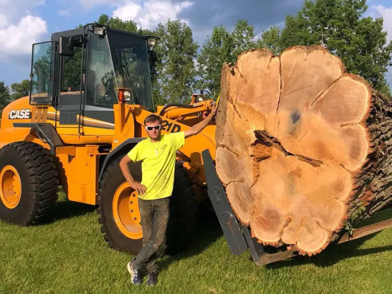Tip Top Timber Co. crew member standing with a wheel loader and a large log round