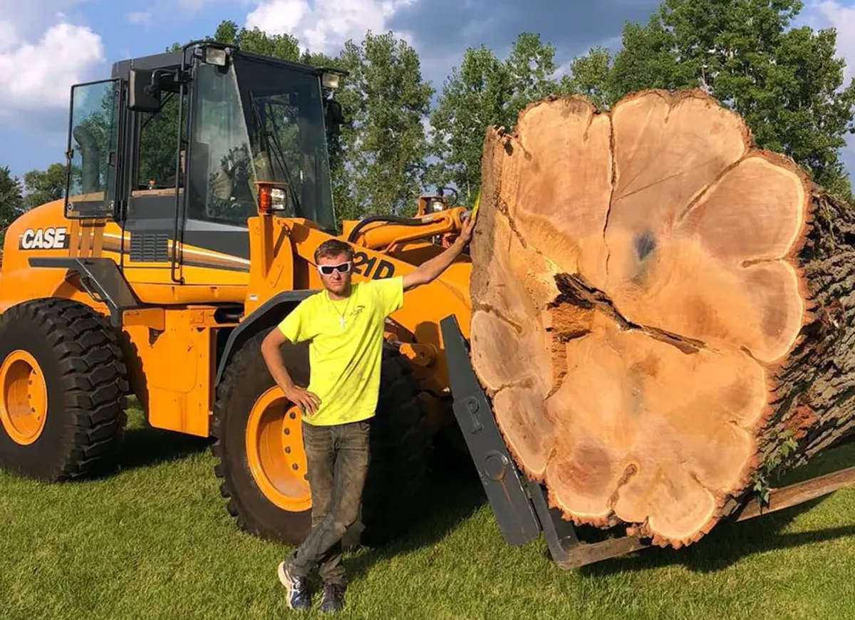 Tip Top Timber Co. crew member standing with a wheel loader and a large log round